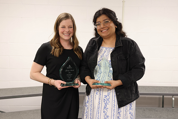 Two staff members stand with awards they received